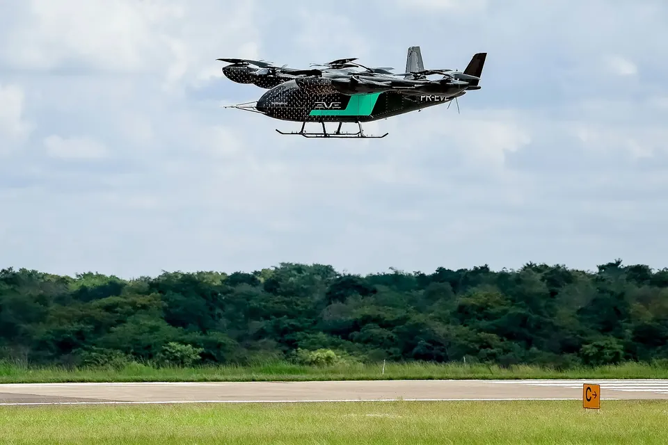 Black and green Eve eVTOL prototype hovering above a grass airfield